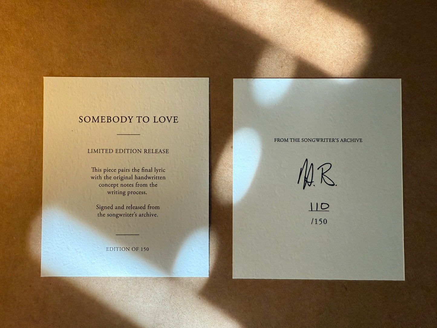 Two limited edition release cards on a textured surface with sunlight casting shadows.